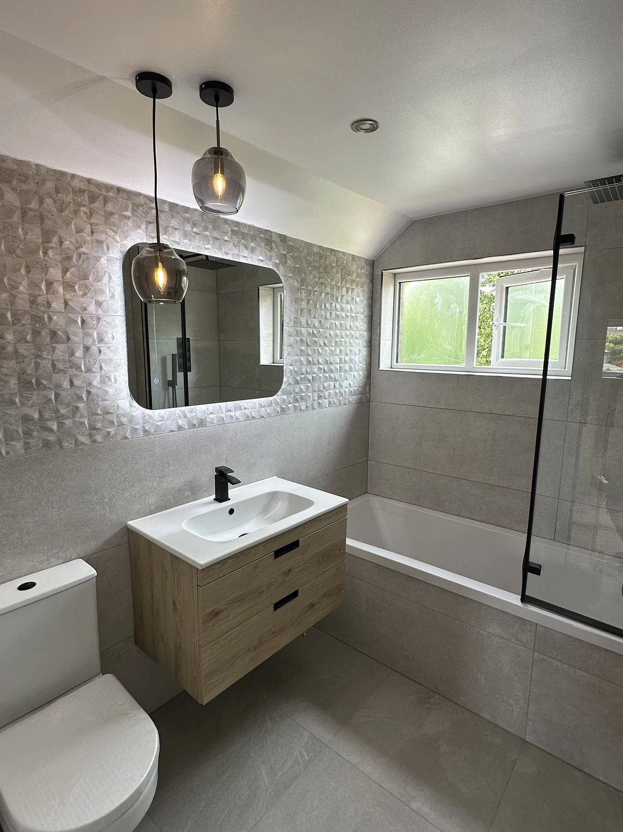 Warm contemporary bathroom with oak-effect vanity, pendant lighting and stone-effect walls, installed by the team